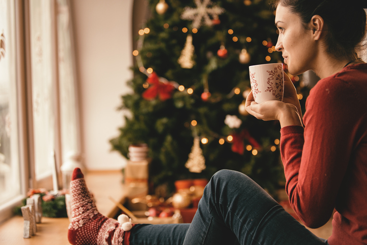 woman drinking tea sitting by the christmas tree, reflecting on the past year